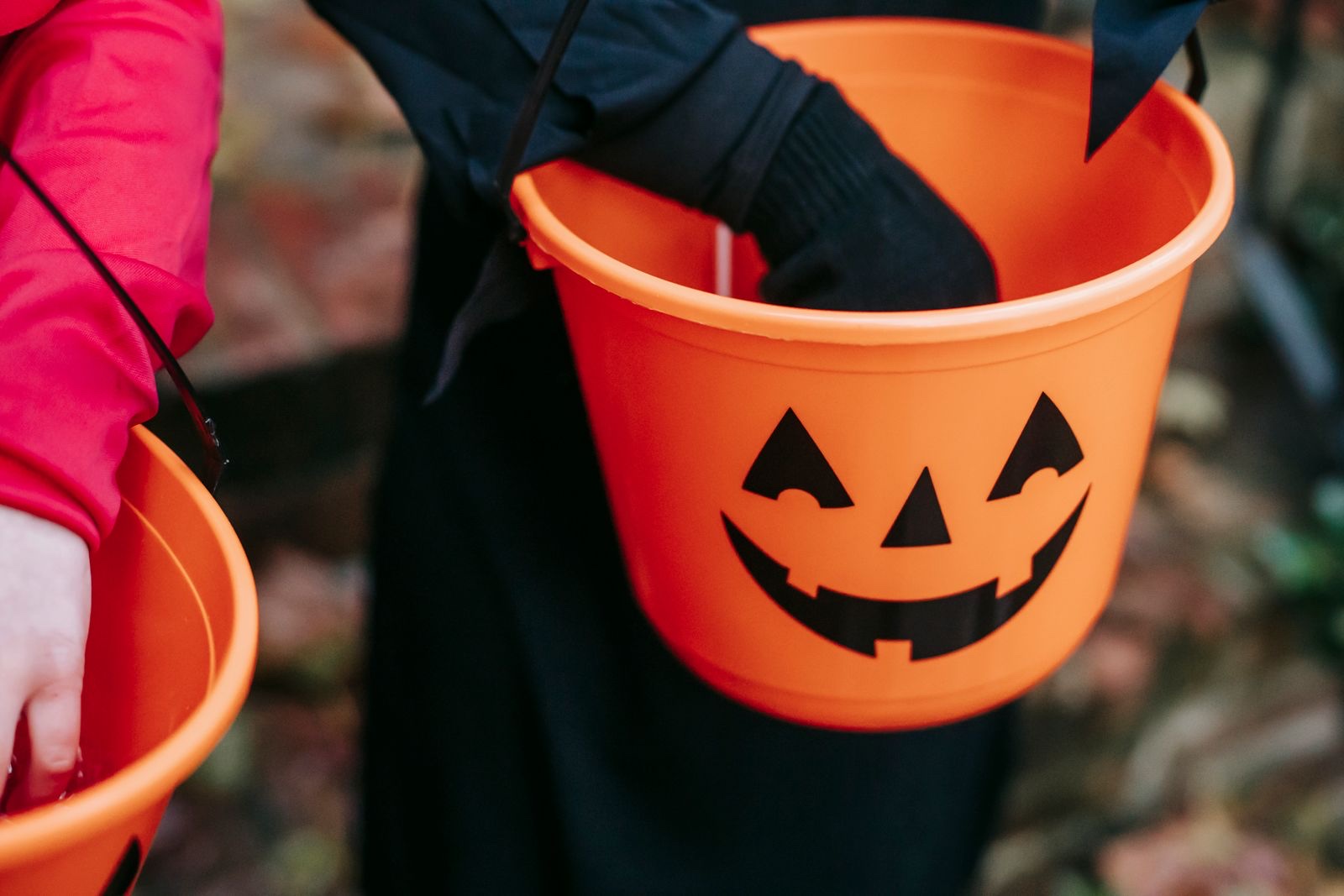 Kids in Halloween costumes holding orange jack-o-lantern candy buckets