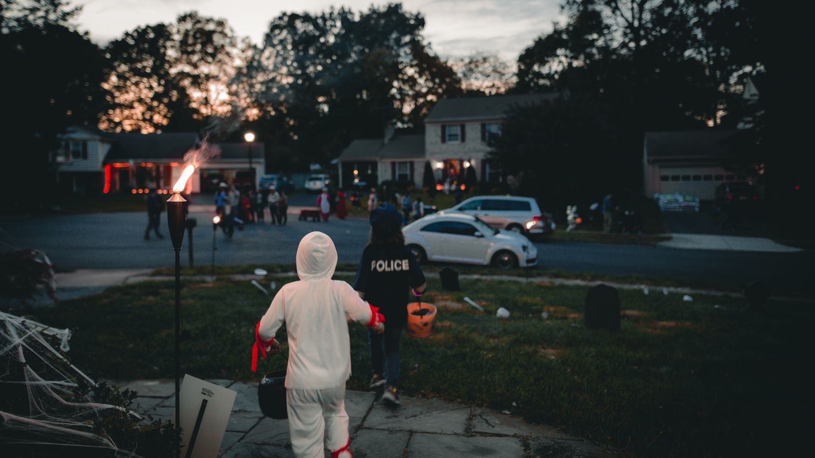 Kids in costumes carrying candy buckets head out trick-or-treating on a suburban street at dusk