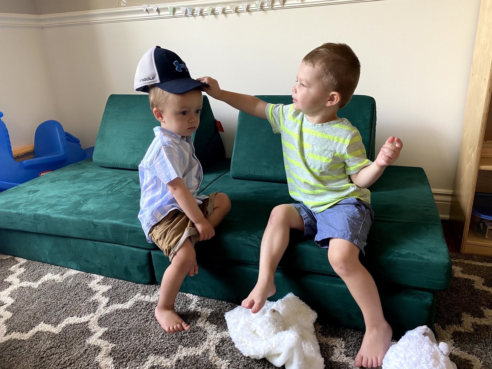 Two young boys sitting on a green Nugget play couch set up in the standard couch configuration in a playroom